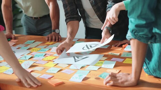 Close up of designer hands design logo graphic together at meeting. Professional graphic working together and brainstorming idea about product design at table with colorful sticky notes. Symposium.