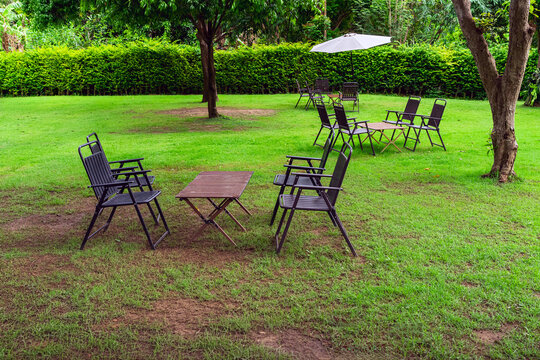 Garden patio set with white umbrella on lush green lawn. 
Outdoor seating area setup featuring woven wicker chairs, round tables, and large white patio parasol placed on vibrant green grass field.