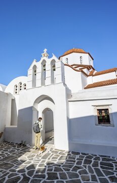 Young man with cat in front of archway with bells of Agios Antonios chapel and Greek Orthodox church Metamorfosi Sotiros, alleys of Marpissa village, Paros, Cyclades, Greece