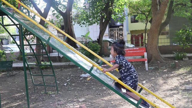 Indian little girls climbing up a playground slide in a public park, enjoying active outdoor play and a fun childhood moment.
