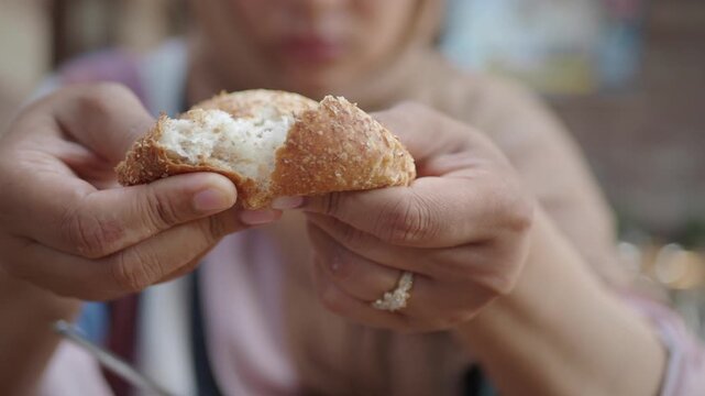 Woman hands breaking fresh crusty bread roll at breakfast table outdoors