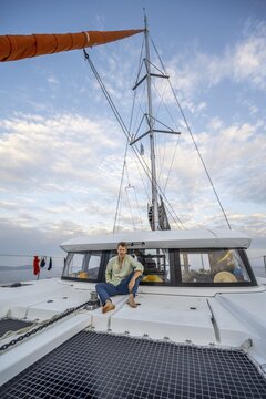 Young man sitting on the deck of a sailing catamaran, sailing trip, Rhodes, Dodecanese