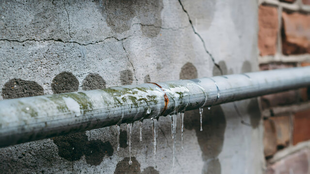 Frozen water pipe with icicles dripping against a weathered brick wall