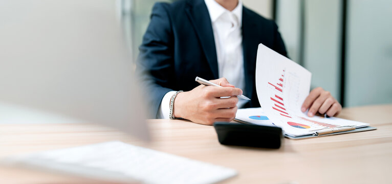 Businessman analyzing financial report graphs and data paperwork at desk in office