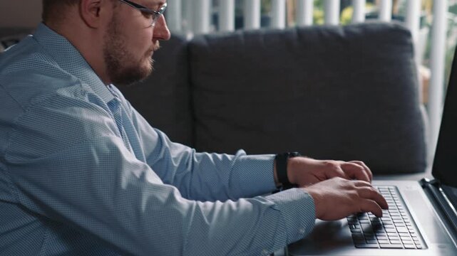 Man typing on laptop working from home on sofa completing online tasks and remote work on computer in calm home environment