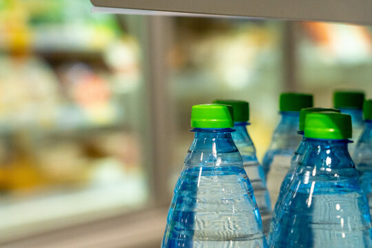 A Close-Up View of Bottled Water with Green Caps in a Chilled Display, Showcasing Refreshing Beverage Options Against a Blurred Refrigerated Background.