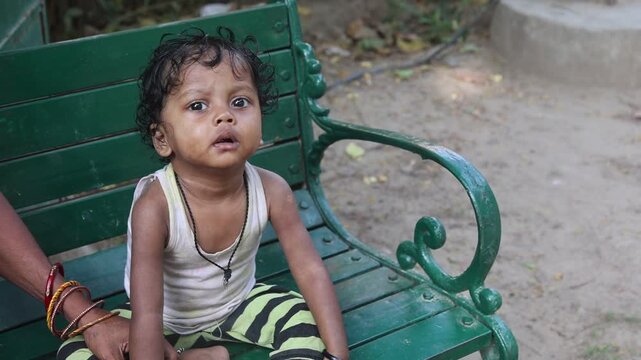 Cute Indian village toddler sitting on a green park bench and looking at the camera, capturing innocent childhood, curiosity, and everyday rural life in India.