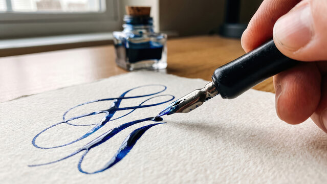 Hand writing elegant calligraphy with a traditional dip pen and vibrant blue ink on textured paper.
