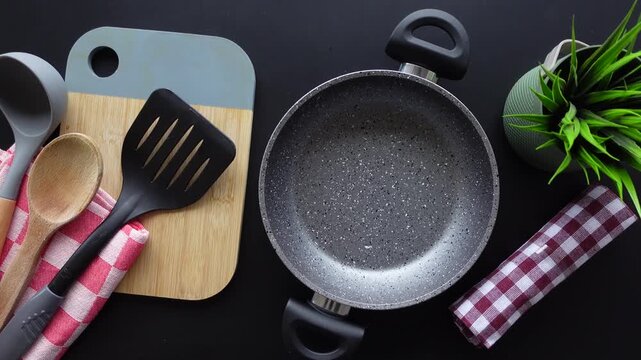 A top-down shot showing different kitchen utensils in a kitchen environment moving into the frame on a black background