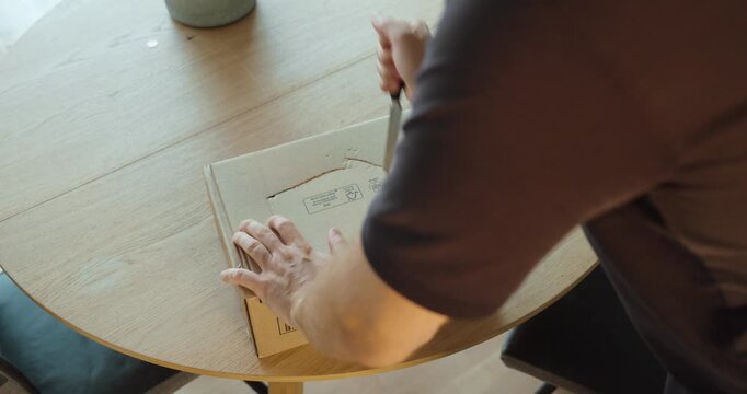 A man opens a cardboard package with a knife, demonstrating unsafe cutting that could accidentally damage the product inside.