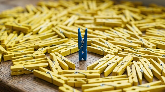 Blue clothespin standing out among yellow clothespins on wooden surface