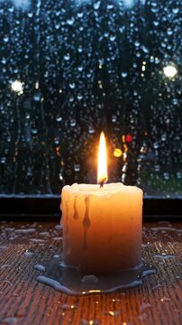 Candle flickering flame melting wax on wooden surface with raindrop water droplets creating calm cozy night light atmosphere