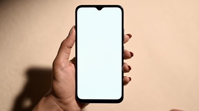 A person's hands hold a smartphone with a blank screen, light falls diagonally
