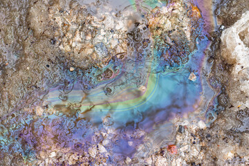 Obraz premium Iridescent oil slick spreading on melting spring snow, chemical pollution pattern creating colorful rainbow reflections on dirty icy puddle surface, environmental contamination closeup
