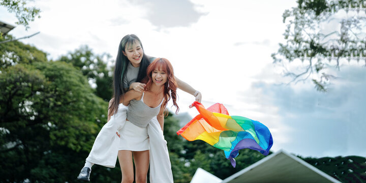 Playful LGBTQ Lesbian Couple Laughing Together with Rainbow Pride Flag Outdoors