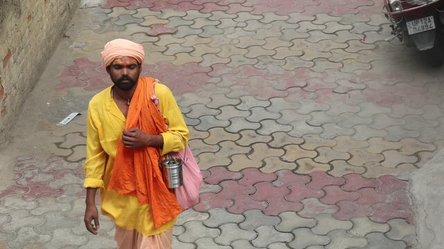 Indian Hindu sadhu walking along a village street in traditional saffron clothing, depicting spirituality, pilgrimage, faith, and everyday rural life in India.