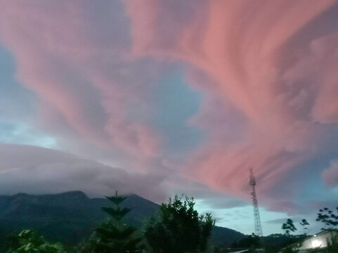Dramatic pink clouds swirl over dark mountains during a scenic sunrise.