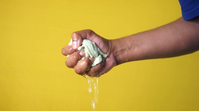 A close up view of person hand squeezing water from a wet fabric, footage of hand wringing out a wet cloth or towel on yellow background