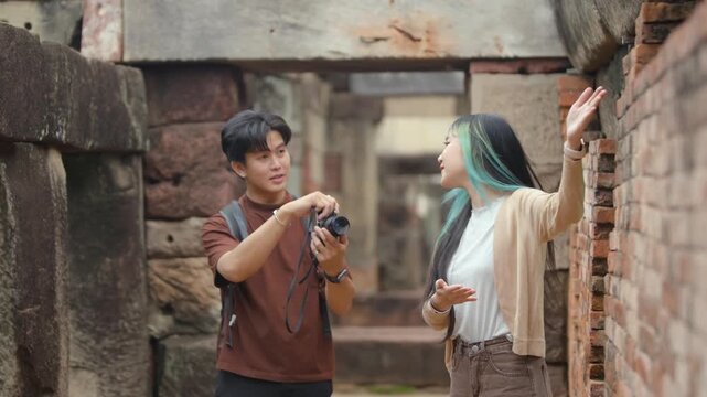 Young Asian tourist couple taking photos and exploring ancient temple ruins together.