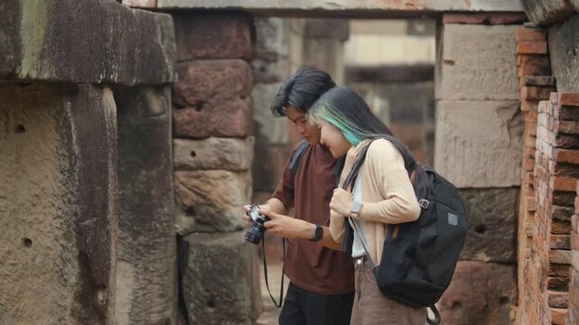Young Asian backpacker couple looking at photos on camera while exploring ancient temple ruins in Southeast Asia
