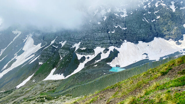 White Abudelauri Lake collects glacial meltwater beneath snow-covered cliffs in Georgia, presenting moraine terrain