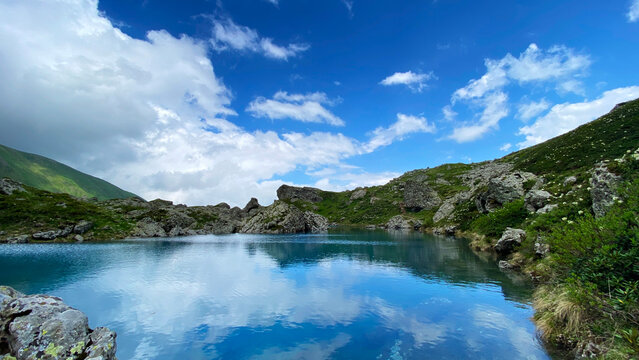 Blue Abudelauri Lake reflects clouds and alpine slopes in Georgia's Caucasus Mountains, combining glacial water