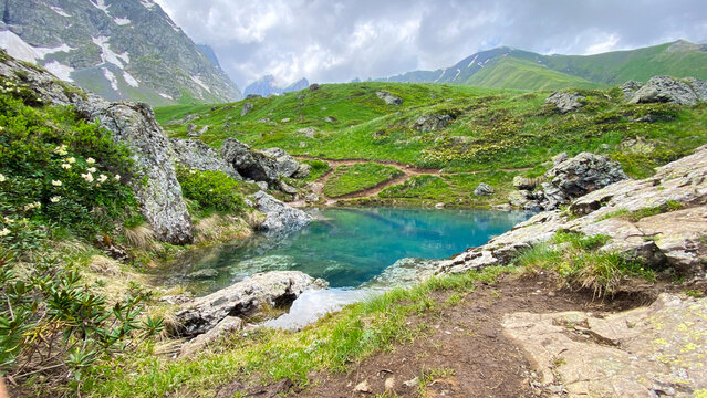 Blue Abudelauri Lake rests among rocky slopes, alpine meadows, and snow patches in Georgia, presenting a remote Caucasus hiking