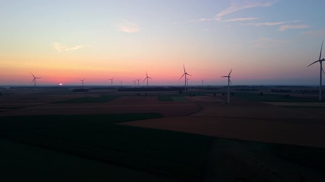Windmill turbines in morning sunrise, sunrise over a field of wind turbines, the sun low on the horizon.