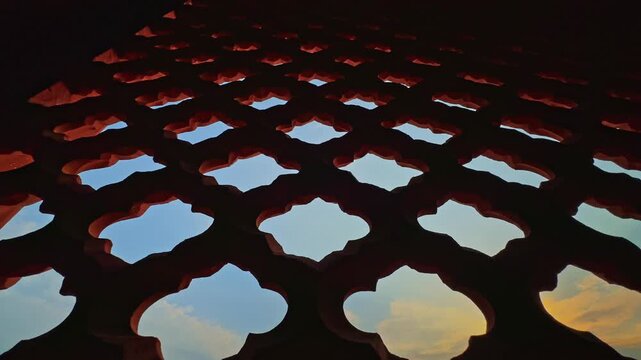 Slow low angle tracking shot beneath an intricately carved sandstone jali window showcasing timeless Indian stone craftsmanship against the open sky