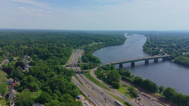Approaching aerial shot toward Connecticut River crossing Julia B. Buxton Bridge and transportation corridor through forested landscape, Springfield, Massachusetts, US