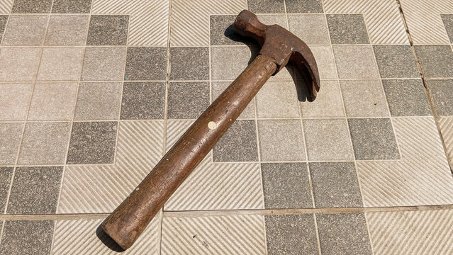 Old Rusty Claw Hammer with Wooden Handle on Ceramic Tile Floor