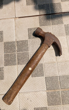 Old Rusty Claw Hammer with Wooden Handle on Ceramic Tile Floor