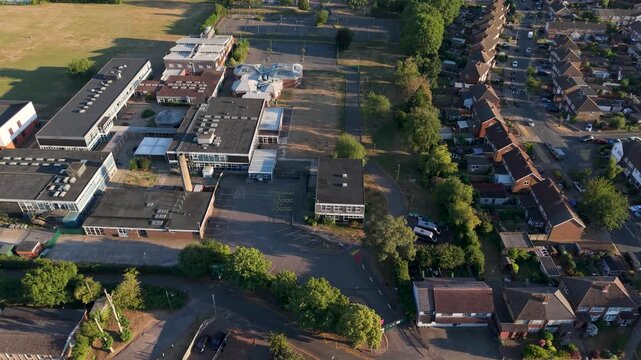 Haileybury Turnford School campus in Cheshunt, Hertfordshire, UK, seen from above as the camera pans left over buildings, sports courts, and fields in warm evening light.
