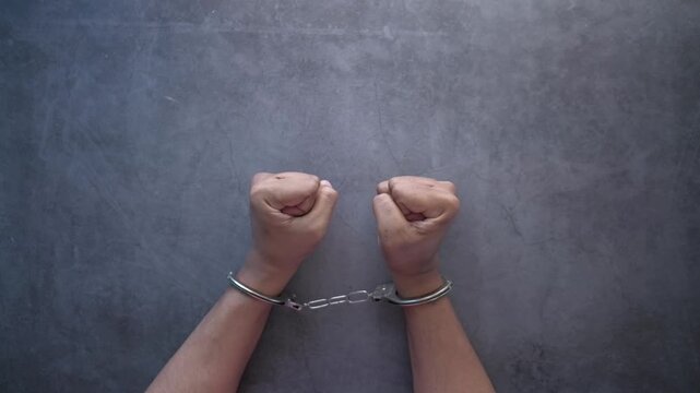 Hands in handcuffs struggle and move on dark textured background, arrest and crime concept footage