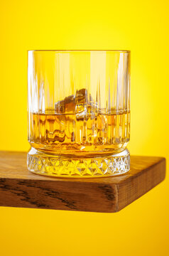 Whiskey glass with ice on yellow background minimal drink still life
