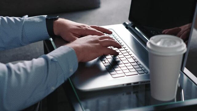 Man typing on laptop takes sip of coffee and continues working on computer completing online tasks and remote work in calm home environment