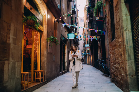 Smiling woman walking on old city street using smartphone. Tourist traveler exploring urban town using mobile application, navigation map, digital nomad lifestyle, authentic representation