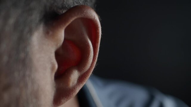 Close up view of middle aged man ear with red light reflecting inside canal showing anatomical details in dark studio