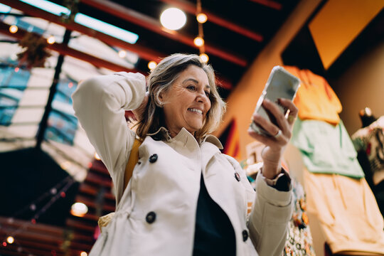 Joyful mature woman looking at smartphone screen in city market, middle aged person enjoying mobile digital content, authentic portrait of tech savvy female using high speed internet app.