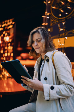 Focused lady working on tablet with stylus pen sitting in cafe evening lights, mature freelancer using digital device for creative design or project, online banking, professional remote task, tech