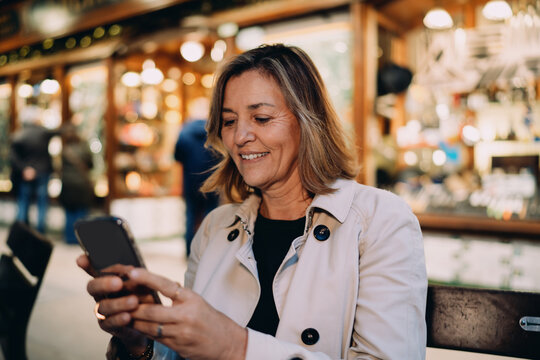 Mature woman checking smartphone notification outdoor, smiling Caucasian lady typing message mobile app, digital lifestyle connectivity, social media influencer blogging, wireless internet technology