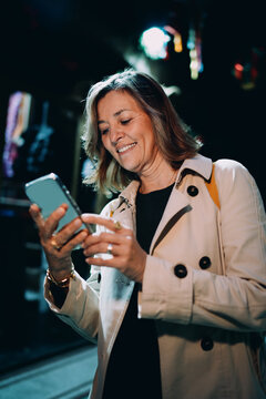 Smiling mature woman browsing smartphone outdoor evening, Caucasian model using mobile application, digital nomad remote work, 5G internet wireless technology, online shopping and banking app