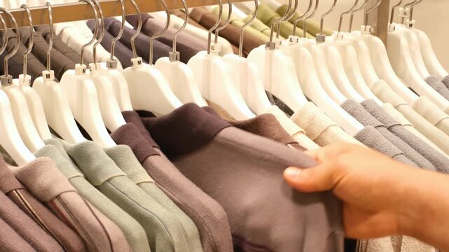 Man chooses clothes hanging on hanger in store.