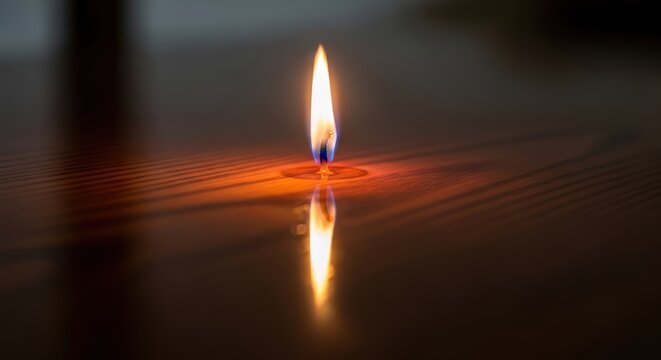 Single candle flame reflecting on a dark, polished surface.
