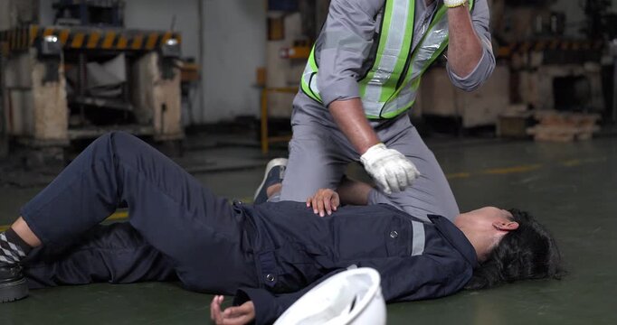  Worker helping injured colleague who collapsed on the floor after accident in factory