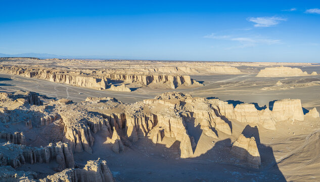 Aerial view of vast yardang landforms with clay formations in the desert under a blue sky, Dahaidao, Xinjiang, China