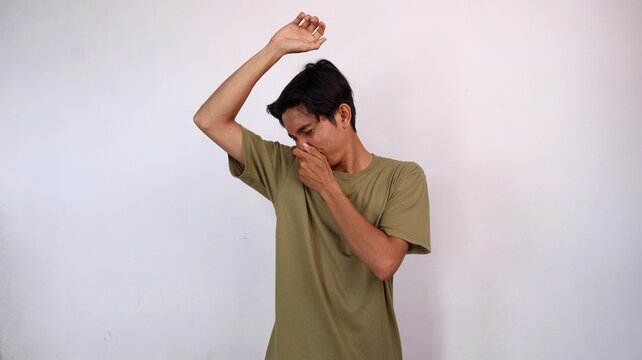Asian young man gestures smelling armpit and covering his nose