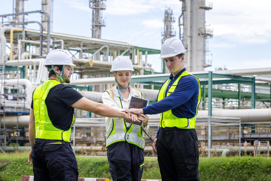 professional industrial engineering team stacking hands together in unity at oil refinery plant, successful collaboration of workers and engineers at petrochemical facility site