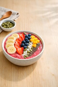 Fresh smoothie bowl with tropical fruit and seeds on light wood table in bright natural light