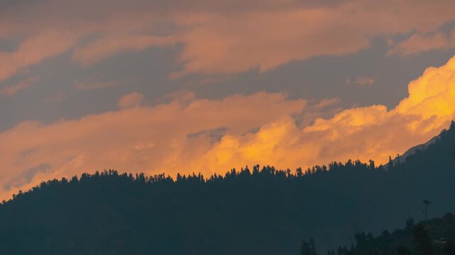 4K Time lapse shot of orange clouds above the Himalayan mountain range with Pine trees during the sunset in monsoon season as seen from Manali in Himachal Pradesh, India. Scenic sunset background.